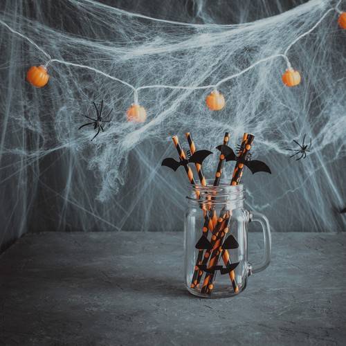 Halloween decorations. A glass jar with drinking straws on dark background with cobwebs.